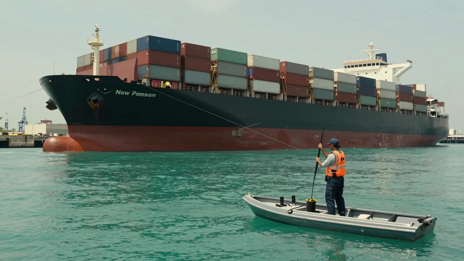 Un buque portacontenedores en un puerto con una embarcación pequeña y un trabajador en primer plano.